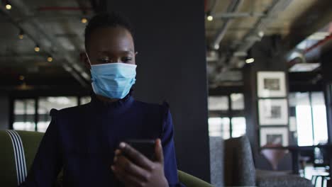 African-american-woman-wearing-face-mask-having-a-video-chat-on-smartphone-at-modern-office