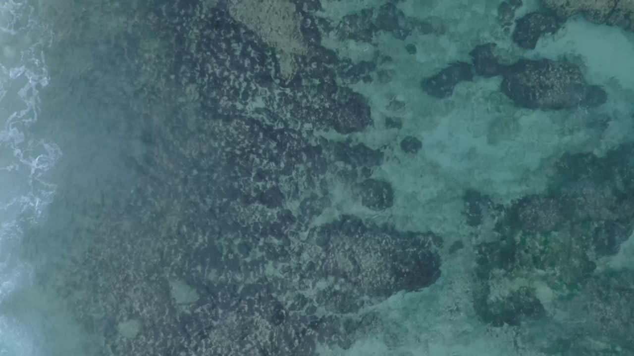vista desde arriba de drones del agua clara turquesa y las olas que se estrellan sobre el arrecife de coral poco profundo en uluwatu bali, indonesia