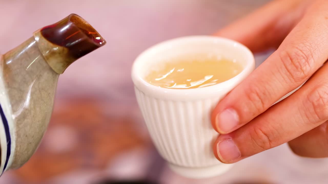 A detailed view of tea being poured into a small, ribbed white cup, highlighting the gentle flow and hand interaction.