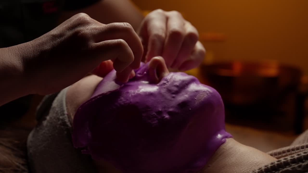 Esteticista retirando mascarilla facial morada del rostro de una mujer en un spa
