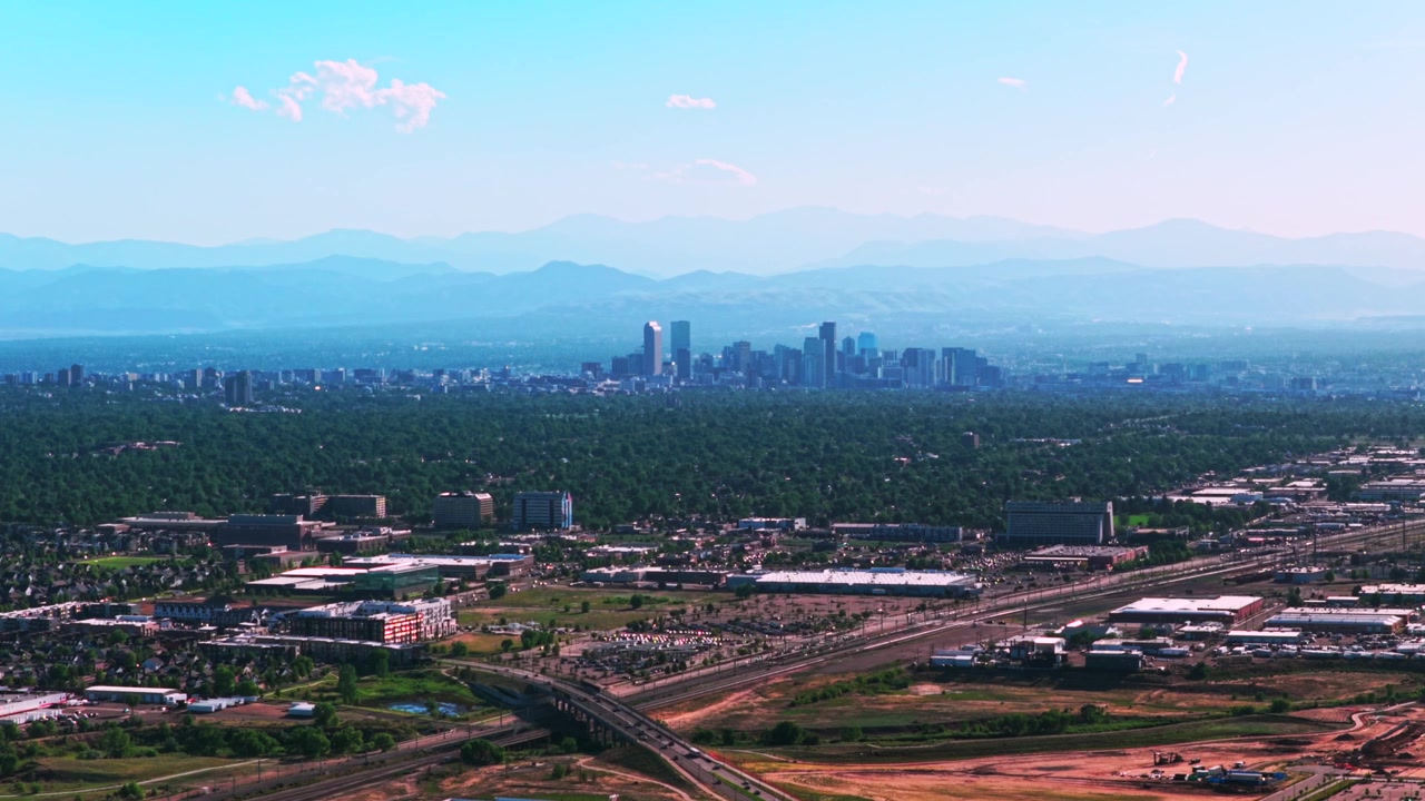 Luftfoto fra drone af Denvers centrum med skyskrabere og bygninger, et bybillede i Colorado. Biler, trafik, forbjerge til Front Range og Rocky Mountains i lag. Sommer, forår, blå himmel, morgen med røgfyldt dis.