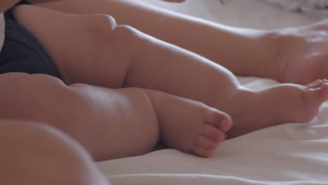 bebé moviendo los pies en la cama mientras la madre lee un cuento - primer plano