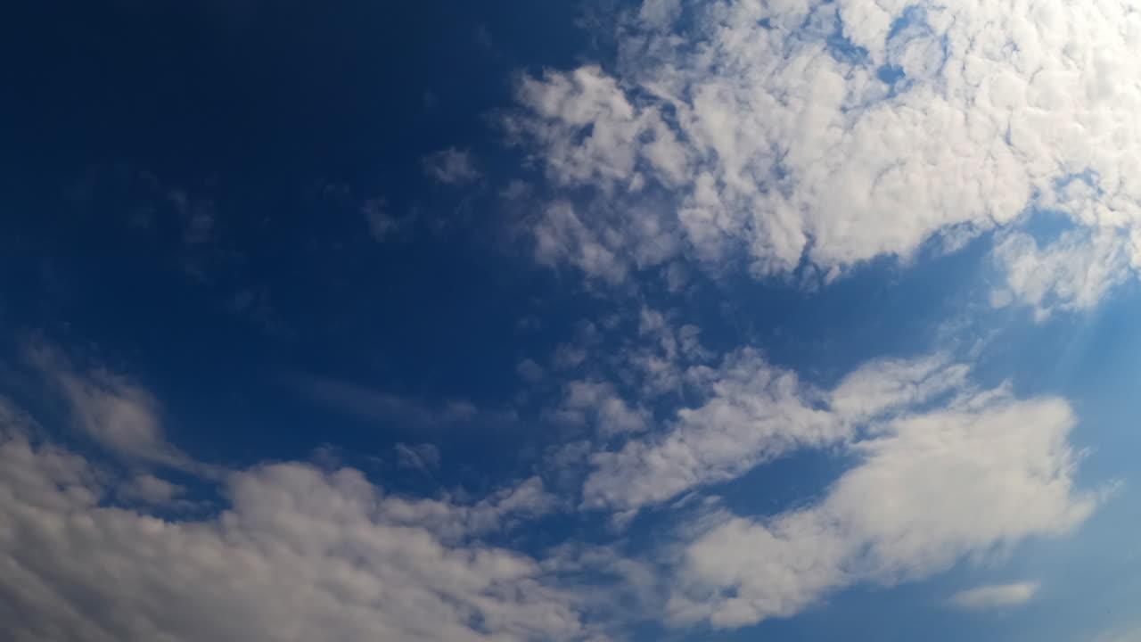 Amazing azure sky with flowing white light clouds. Low angle view at the summer sky on a sunny day. Timelapse