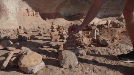 precision and balance: hand placing a rock on stone pyramid in a sunny sandy environment