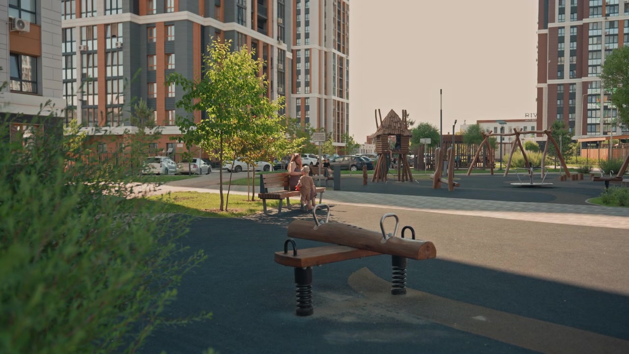 Woman and young boy interact in public park with playground equipment tall apartment buildings visible beyond. scene features natural daylight lighting green foliage framing foreground
