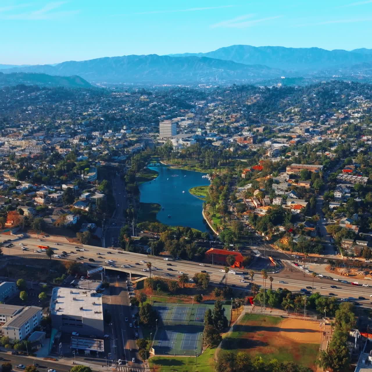 Approaching the beautiful little lake in the residential area of Los Angeles. Busy traffic in the green part of the city at backdrop of mountains