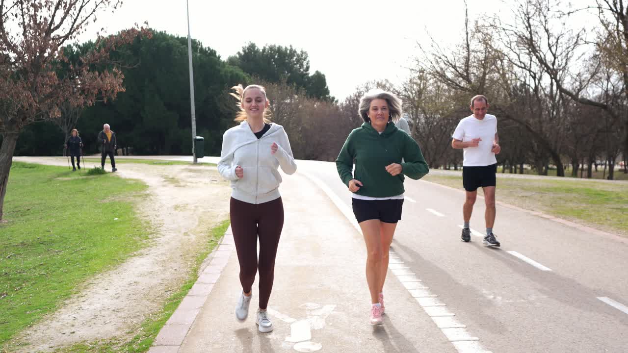 Gruppo eterogeneo di persone che fanno jogging insieme su un sentiero asfaltato in un parco