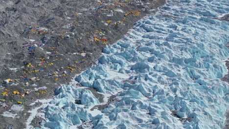 Close-up drone shot of Everest Base Camp and Khumbu Glacier, Nepal in dense snow, melting ice, Sagarmatha peaks, high-altitude tents, layered Himalayan mountains under sunny skies, adventurous travel