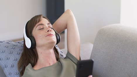 caucasian woman enjoys music with closed eyes, wearing white headphones