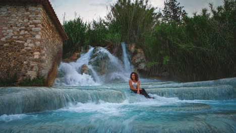 Cinemagraph-De-4k-Uhd:-Bucle-De-Video-Continuo-De-Una-Mujer-Joven-Sentada-Frente-A-Una-Cascada-De-Aguas-Termales-En-Saturnia,-Italia