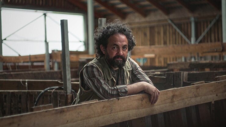 Portrait of Male Farmer Leaning on Wooden Cattle Pen Fence inside Barn