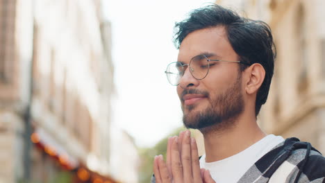 religious indian man praying with closed eyes to god asking for blessing while standing on street