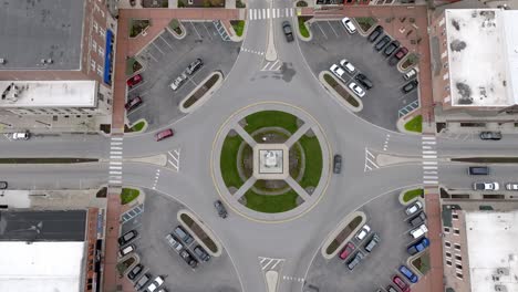 Angola,-Indiana-town-square-roundabout-with-cars-moving-around-and-drone-video-moving-down