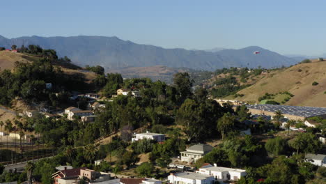 Helicopter-dropping-water-on-California-brush-fire,-Los-Angeles-suburb,-aerial-view