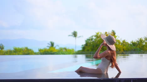 Jovencita-Sexy-Sentada-Cerca-De-La-Piscina-Remojándose-Los-Pies-En-El-Agua-Mirando-Alrededor-Y-Disfrutando-De-Sus-Vacaciones