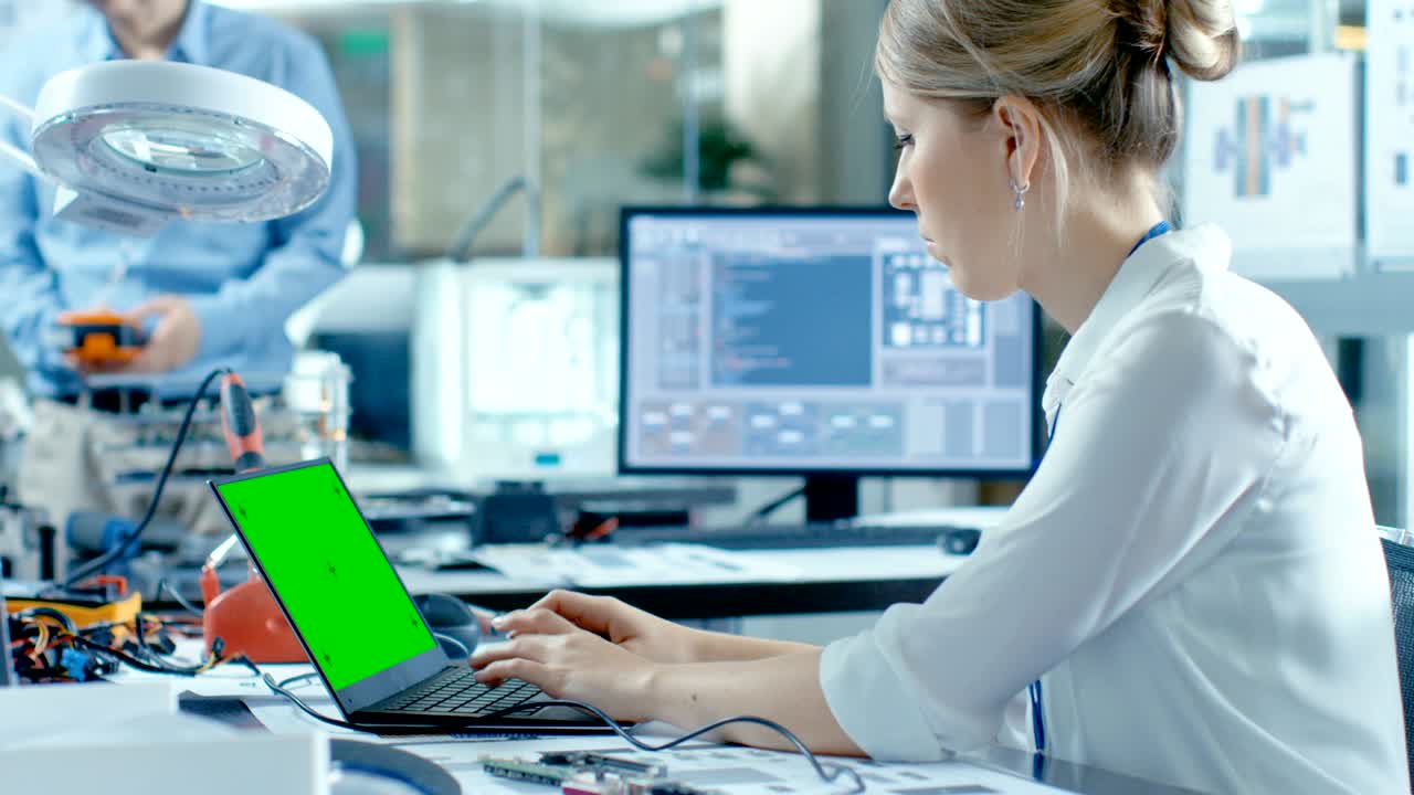 женщина-компьютерный ученый подключает плату к своему ноутбуку и начинает программировать ее. она работает в технологически продвинутой лаборатории.