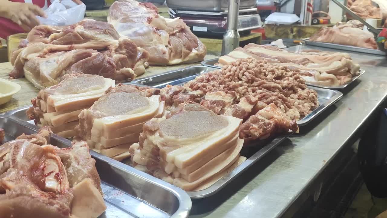 Pork in a wet market is typically displayed fresh, red, and glistening, often hanging on hooks or arranged on tables.