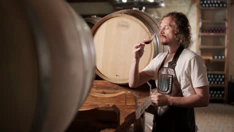 authentic shot of successful male sommelier is tasting a flavor and checking white wine quality poured in transparent glass in a wine cellar.