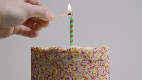 studio shot of revolving birthday cake covered with decorations and single candle being lit 2