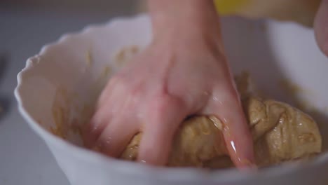 female kneading brown dough with fer hand until it becomes one whole into a white bowl