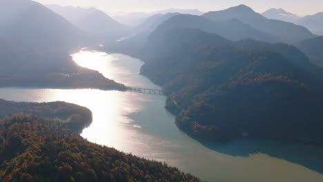 Luftaufnahme-Umkreisende-Alpine-Waldberge,-Die-Sich-Bei-Sonnenaufgang-Im-Schimmernden-Sylvensteinsee-Spiegeln