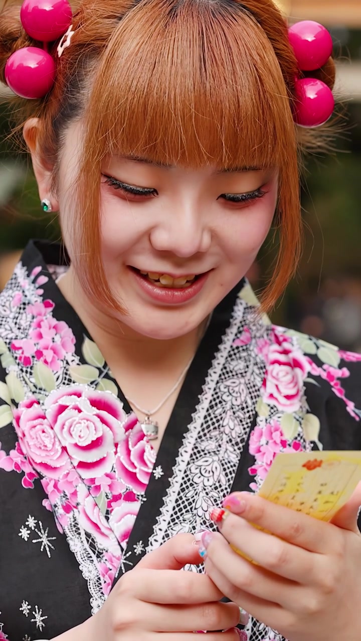 Primo piano di una donna giapponese sorridente in kimono tradizionale che legge un biglietto della fortuna a Tokyo