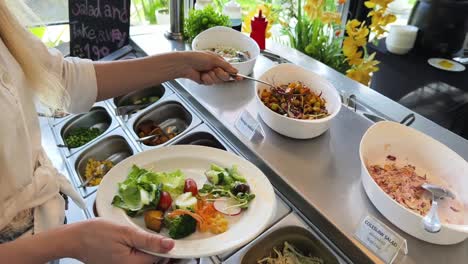 woman serving herself a salad at a buffet restaurant.