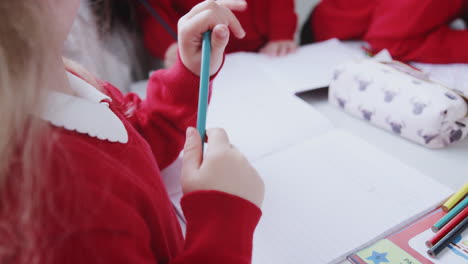 young white schoolgirl drawing at desk in an infant school classroom, close up, over shoulder view