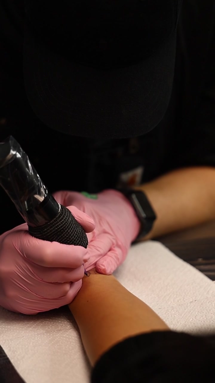 Tattoo Artist Using Machine to Ink Design on Client Arm