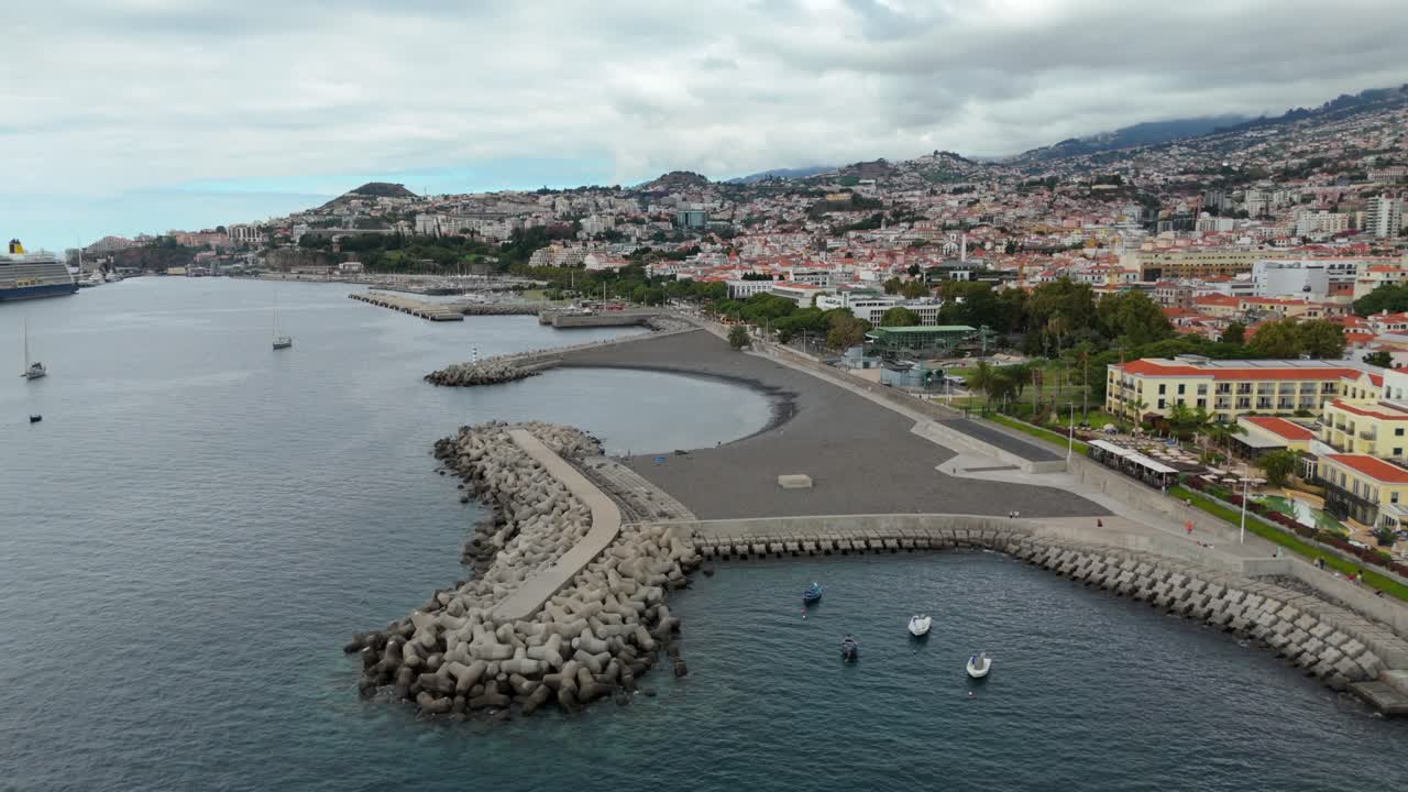 Ripresa aerea con drone in panoramica della costa della baia di Funchal con costa frangiflutti rocciosa e lungomare, Madeira