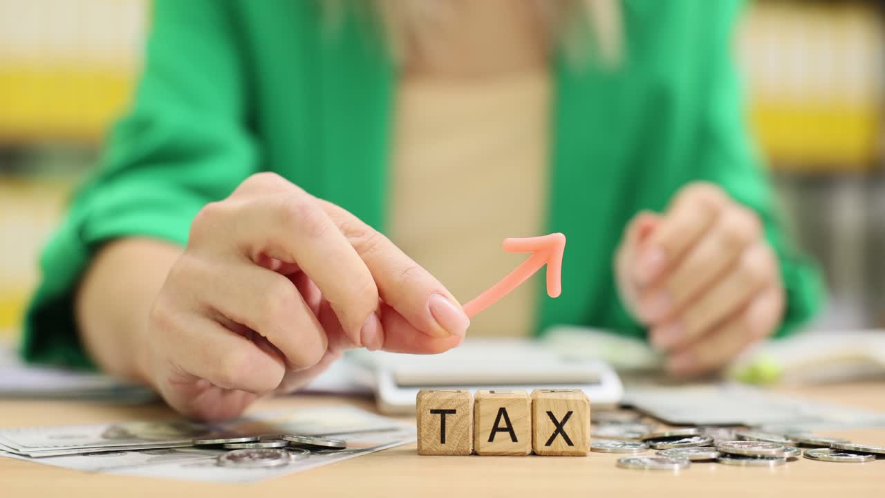 Wooden blocks form word tax on table near scattered coins