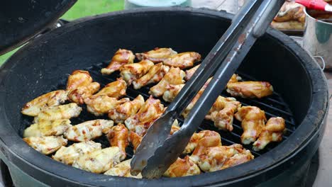 tongs flipping chicken wings with bbq sauce cooking on a kamado style ceramic grill