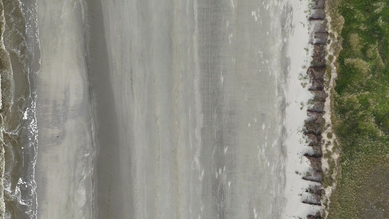 Vertical aerial view over surf,wide beach,dune landscape and coastal protection.