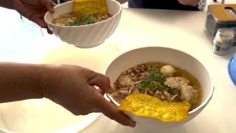 hands serving noodle soup with toppings