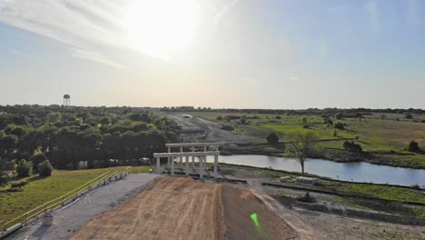 Volando-Hacia-Abajo-Y-Bajo-Hasta-La-Superficie-De-Una-Carretera-En-Construcción-Y-Un-Puente-Sobre-Un-Sitio-De-Conservación-De-Suelo-Acuático