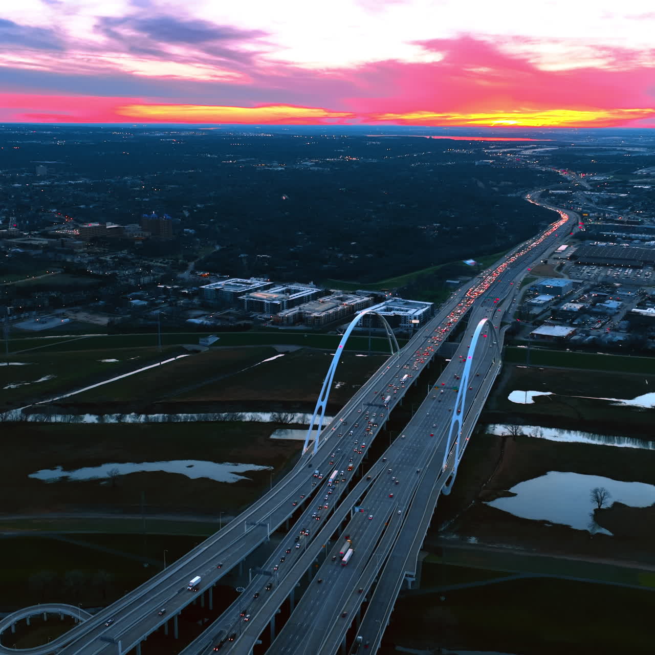 Multiple cars with headlights on move by the Dallas Margaret Mcdermott Bridge at twilight time. Spectacular view of the metropolis from top with colorful sky at backdrop