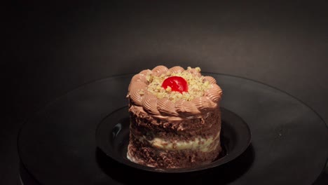 mini petite individual portion slice of chocolate and cheese cake in a turn table with black background with cherry on top and nuts tasty yummy delicious