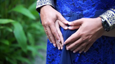 Couple-at-garden-holding-a-pregnant-woman's-belly