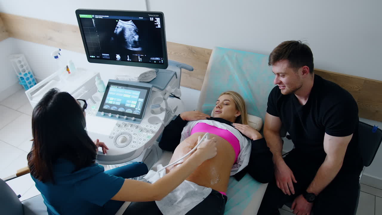 Obstetrician says something to a lady during the ultrasonic check up. Doctor looks at the monitor and explaining it to a patient.