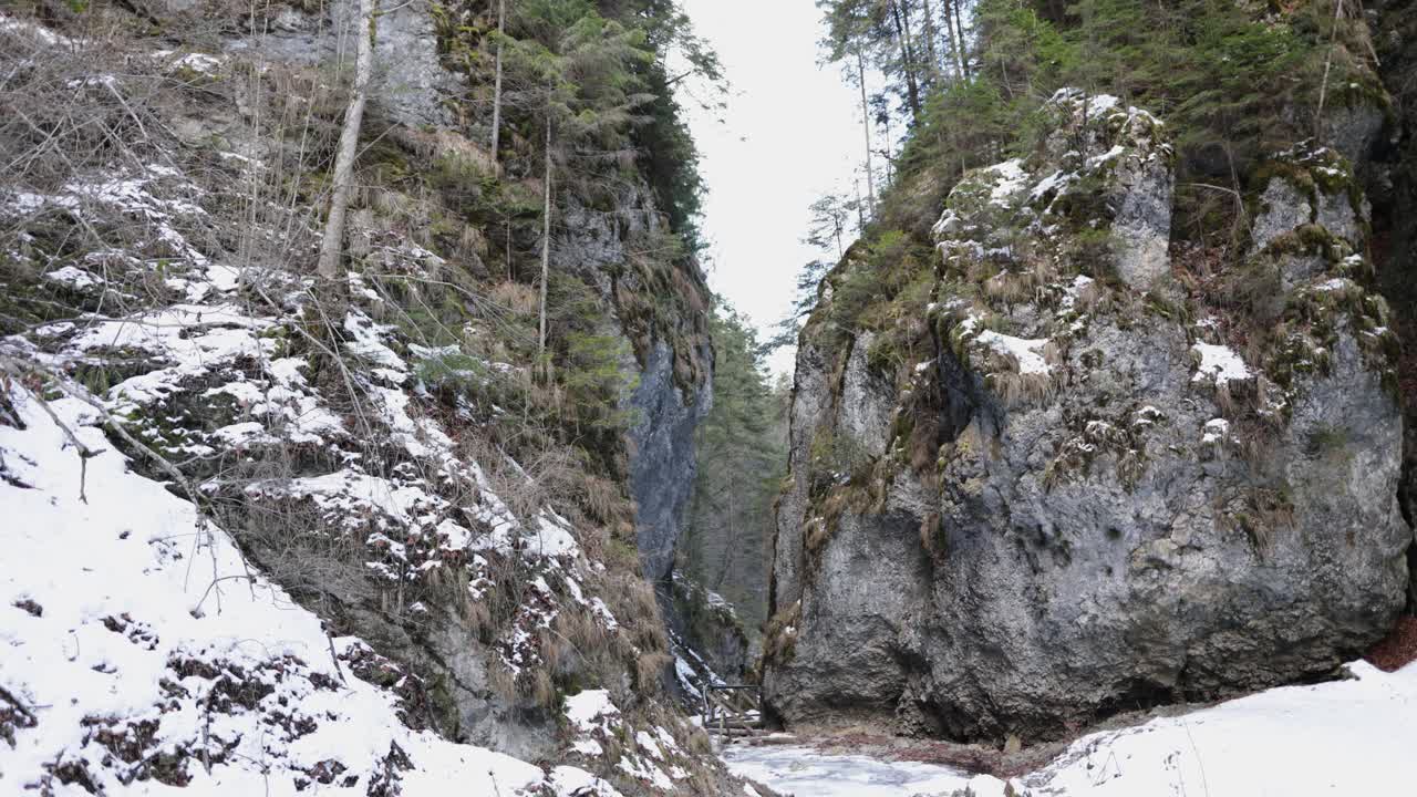 Kapea aukko korkeiden jylhien vuorten välissä lumimetsässä talvella.