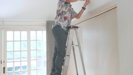 hombre asiático en una escalera instalando una cámara de cctv en la pared para la seguridad