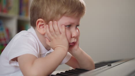 el niño pone los codos en el teclado del piano y se apoya en las manos