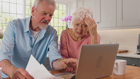 worried retired senior couple with laptop looking at bills at home concerned about cost of living