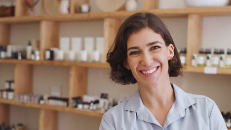 retrato de la dueña de la tienda de regalos de pie frente a los estantes con cosméticos y velas