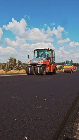process of pressing fresh asphalt on the road in a bright sunny day. two new compactors working on the new road leveling up hot bitumen in summer. vertical video