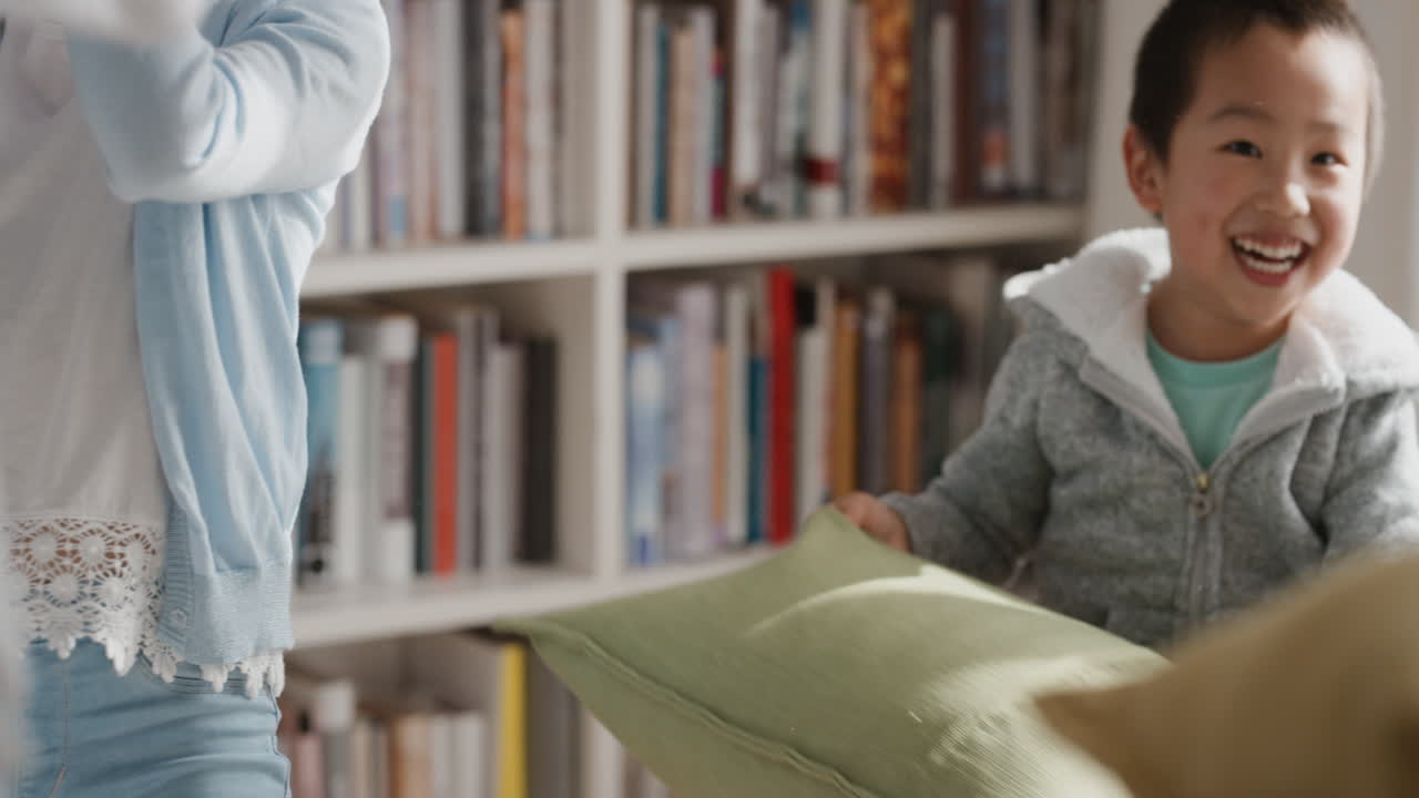 재미있는 작은 아시아 소년 웃고 가족과 베개 싸움을하고 부모와 함께 집에서 미친 게임을하고 함께 재미를 느끼고 4k