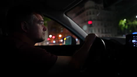 driver in a dark vehicle, focused on the road with illuminated dashboard and city lights outside