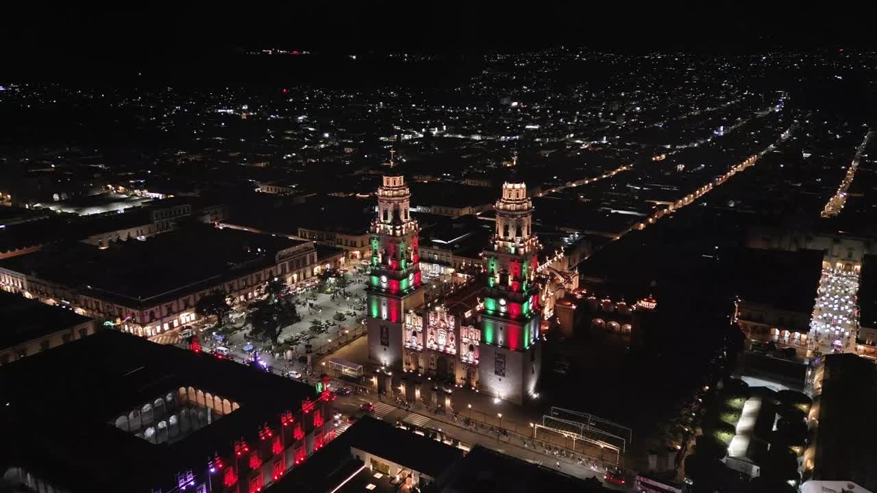 Morelia Cathedral at night, lit with the patriotic colors green, white, and red. Drone shot during the month of September.