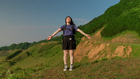 woman backpack trekker raises arms to take in the triumphant beauty of nature, asia lush green valley