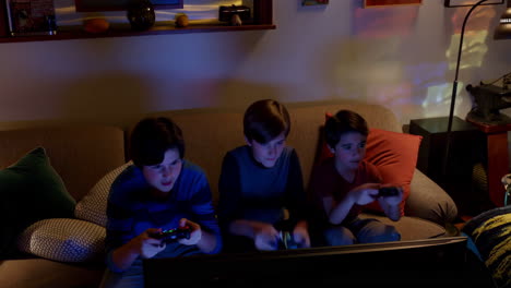 three young boys playing video games together on a couch